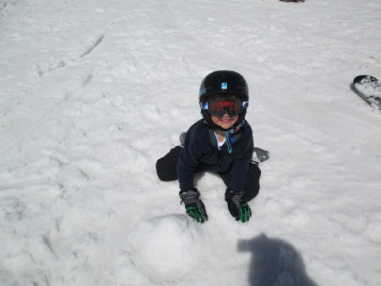 A young boy, enjoying his big bear vacation, blissfully kneels down in the snow.