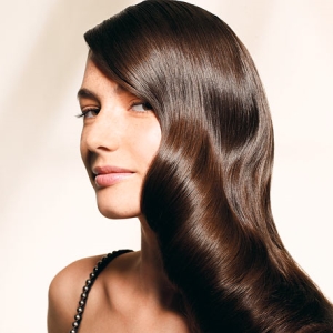 A woman with long brown hair is posing for a photo after receiving a gloss treatment.