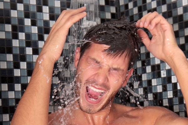A man in a shower with water splashing on his head.