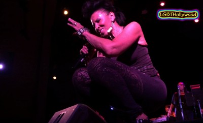 A LGBT woman crouching on stage with a microphone.