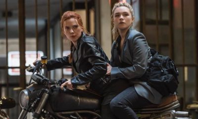 Two women in leather jackets sitting on a motorcycle.
