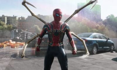 The spider - man is standing in front of a car.